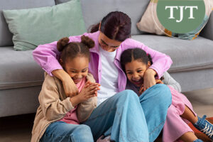 Foster mother laughing with two young girls on the living room floor